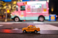 Yellow classic taxi model parked by the pink ice cream truck on a street in New York at dusk